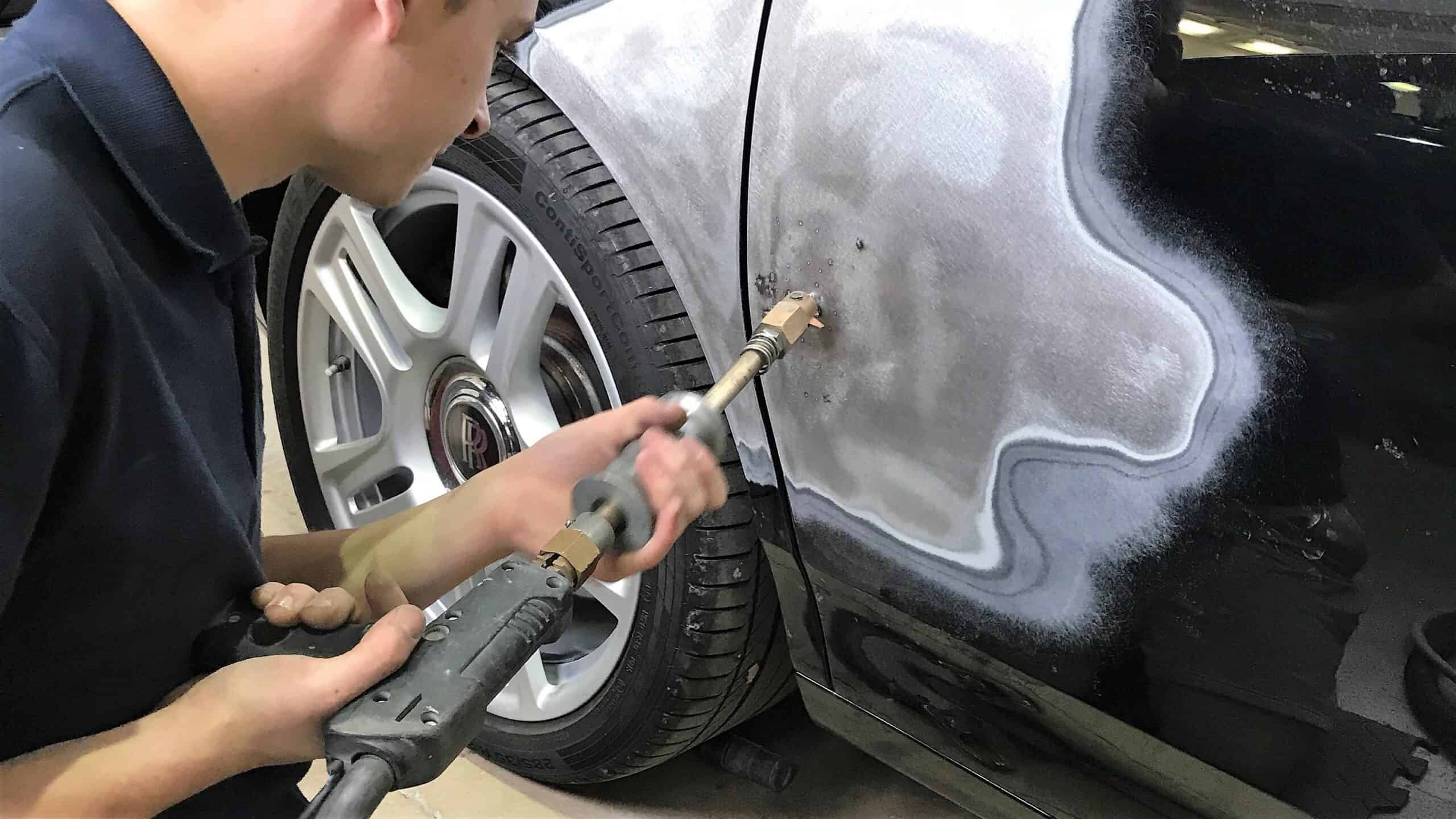 Technician repairing car door after accident with sanding and painting.